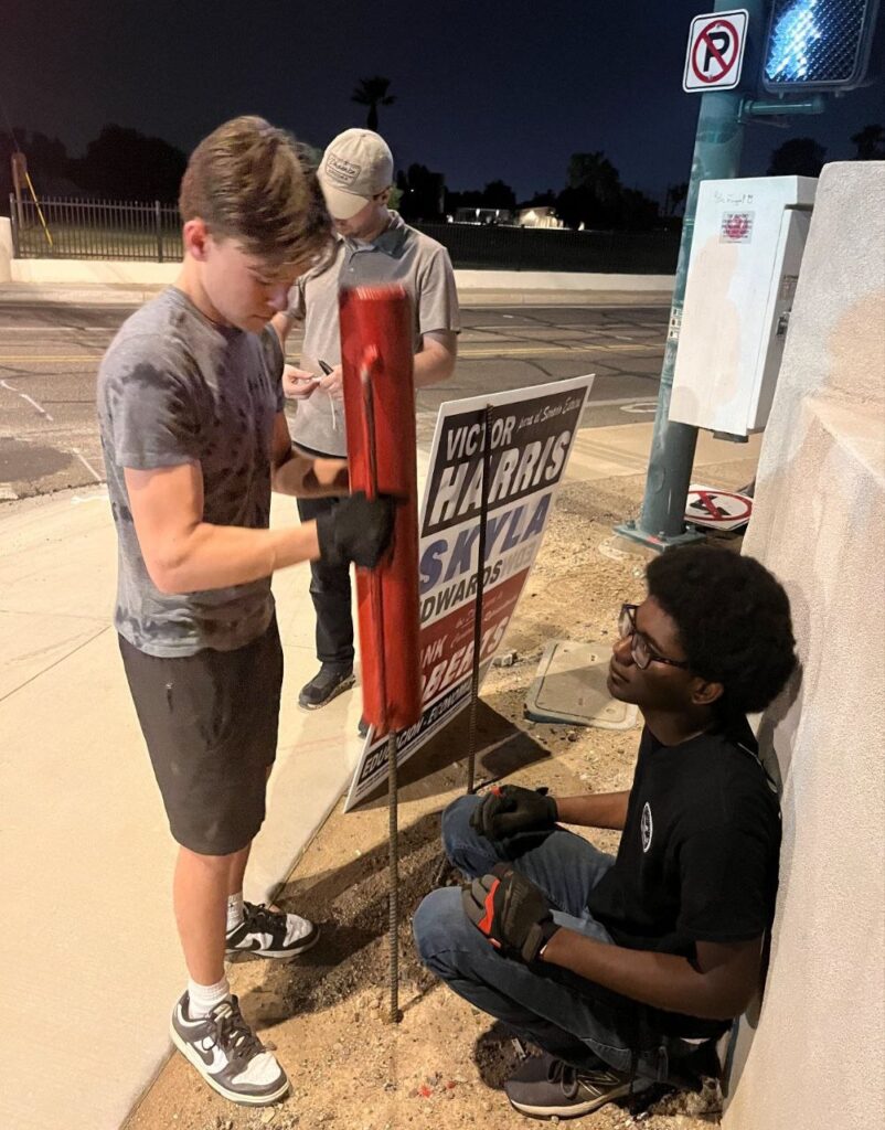Nico Delgado and Isaac Glover pound a campaign sign supporting Victor Harris, Skyla Edwards, and Frank Roberts in LD26.